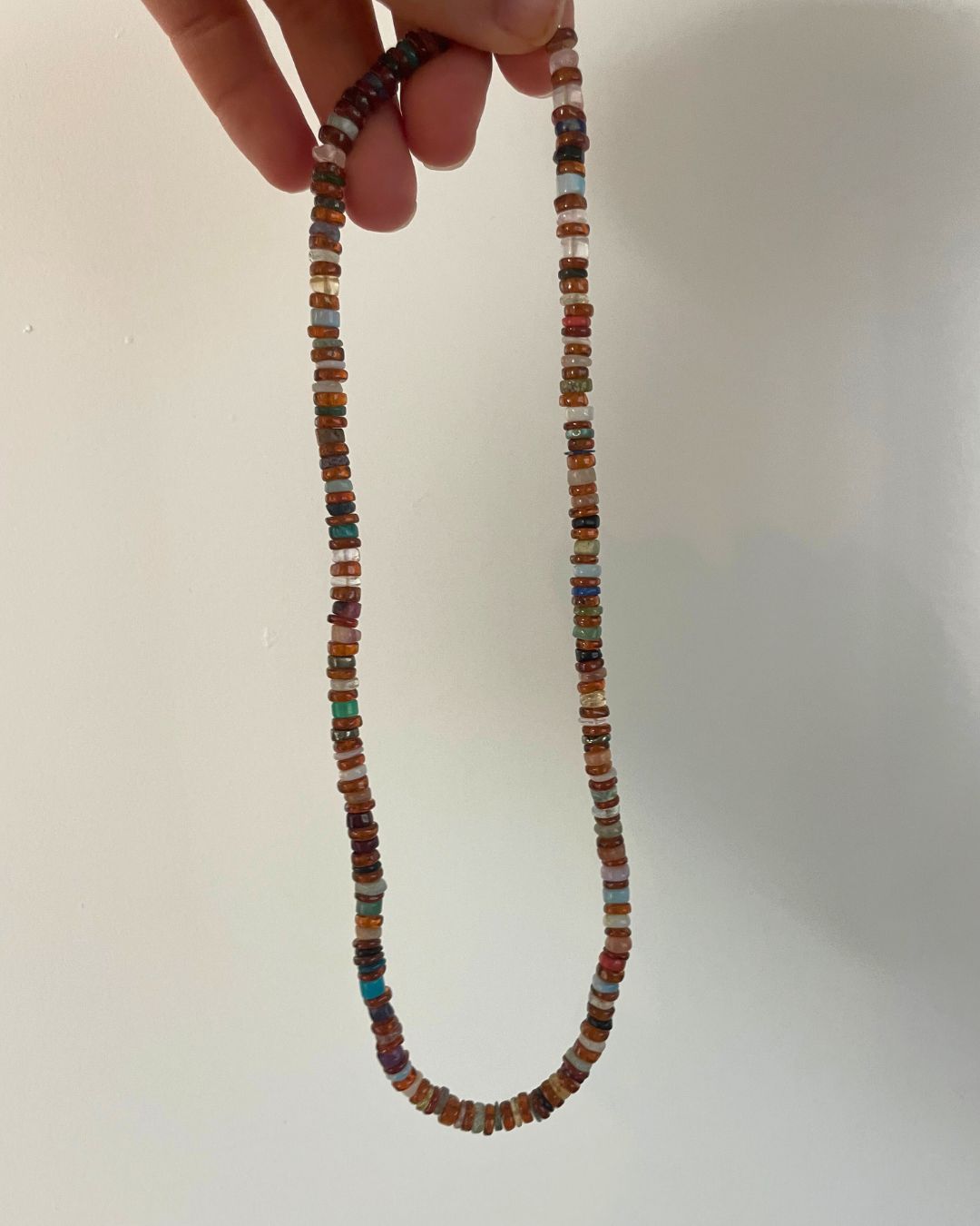 Necklace with multicolored beads held by a hand against a white background