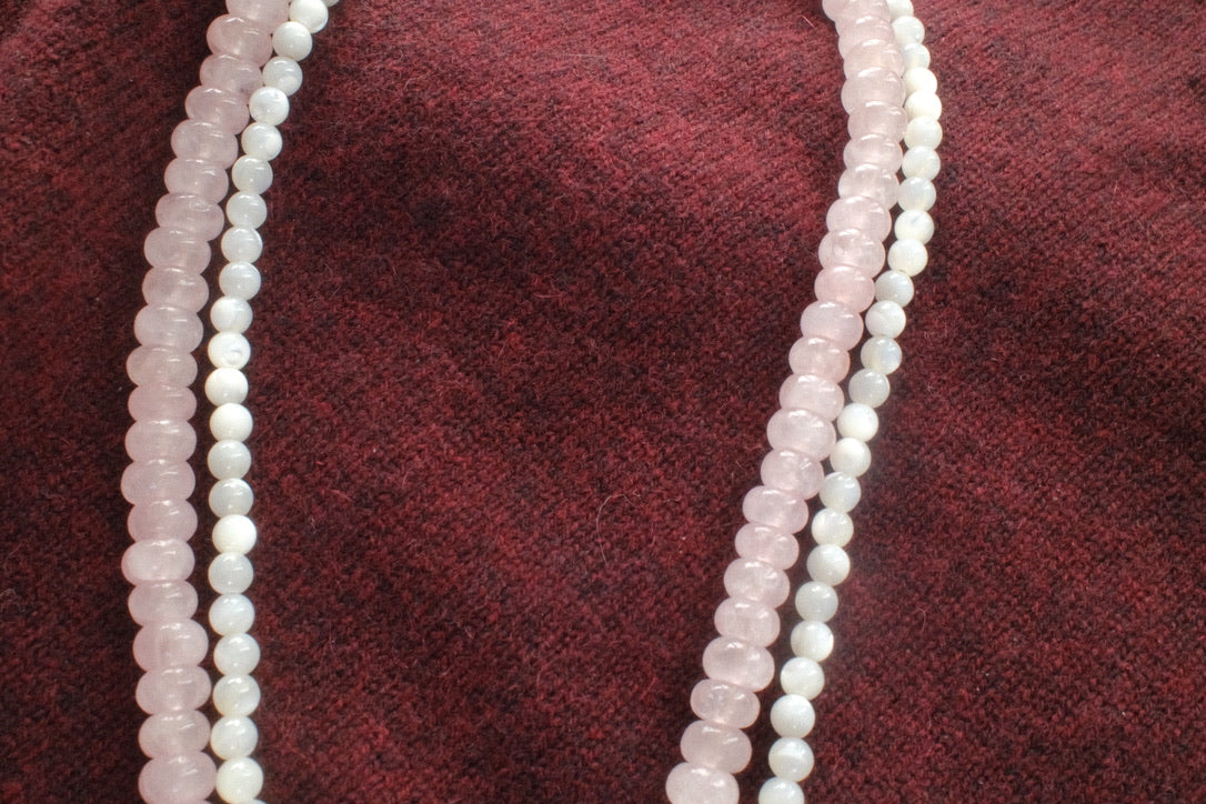 Two strands of rose quartz beads on a maroon fabric background