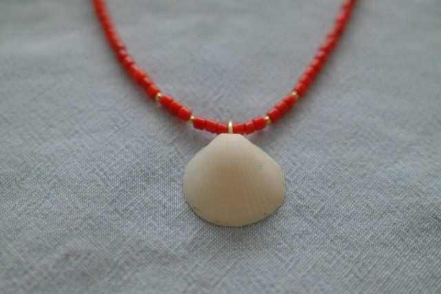 Necklace with red beads and a beige pendant on a light gray fabric background