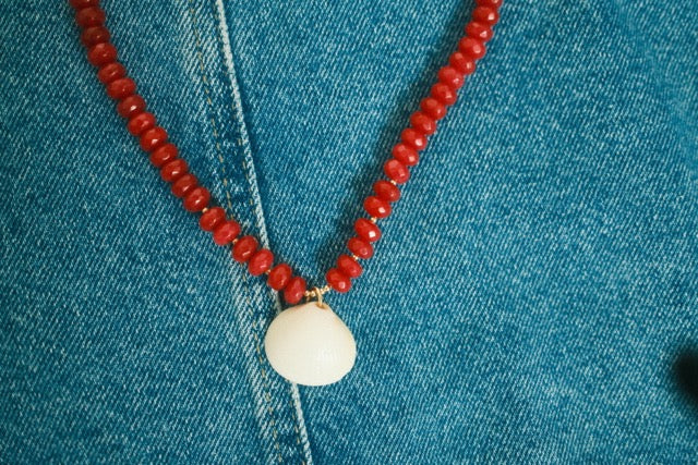 Red beaded necklace with a white pendant on a blue denim background
