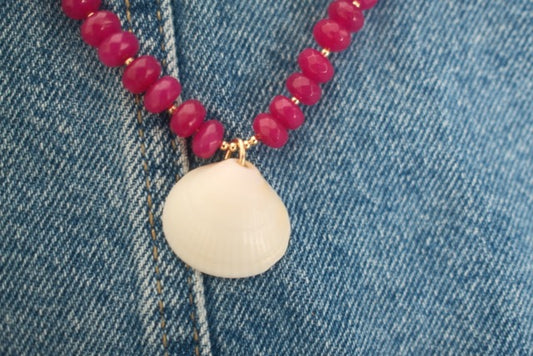 Necklace with pink beads and a white pendant on denim fabric