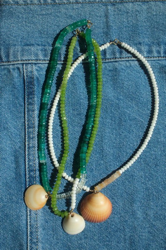 Necklace with green, white, and beige beads and shell pendants on a blue denim background
