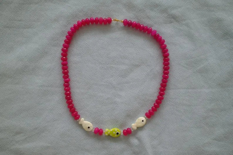 Necklace with pink beads and fish-shaped charms on a light gray fabric background