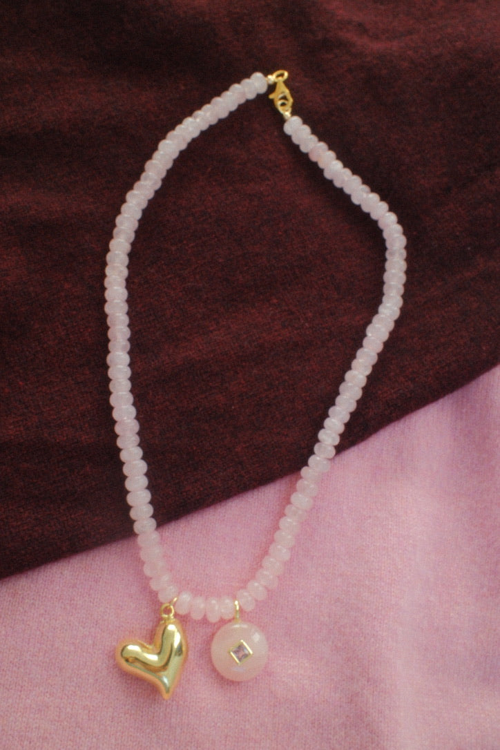 Necklace with heart and square pendant on a wrist against a brown background