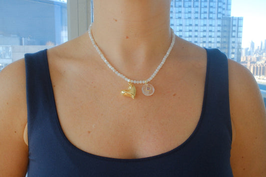 Person wearing a necklace with a bell pendant in front of a window with a cityscape view