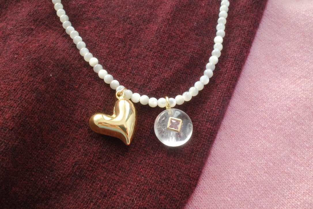 Necklace with heart and round charm on a textured fabric background