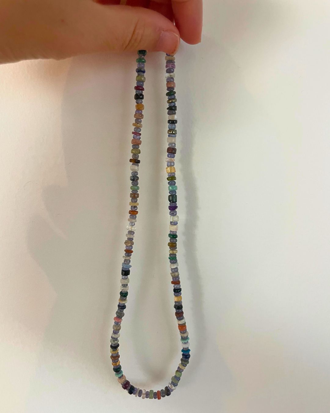 Multicolored beaded necklace held by a hand on a light background