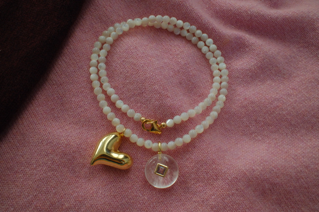 Pearl bracelet with gold heart and clear crystal charm on a pink fabric background