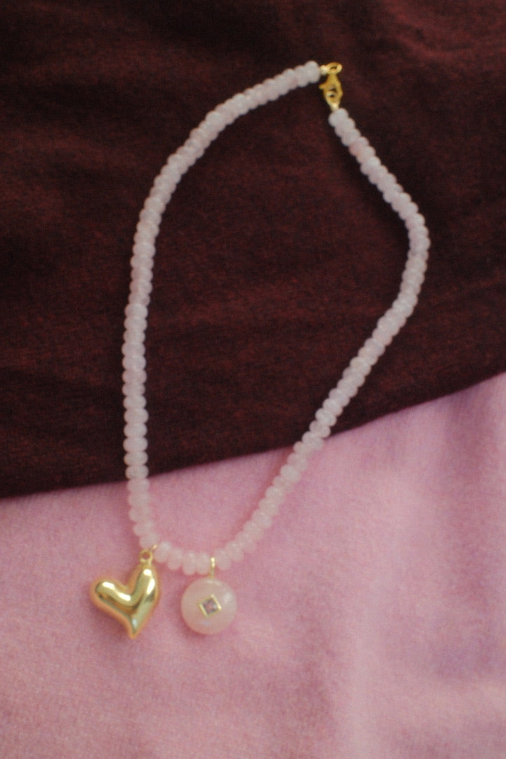 Necklace with heart and pearl pendant on a pink surface