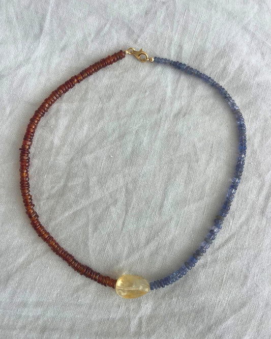 Necklace with red, blue, and gold beads on a light gray fabric background