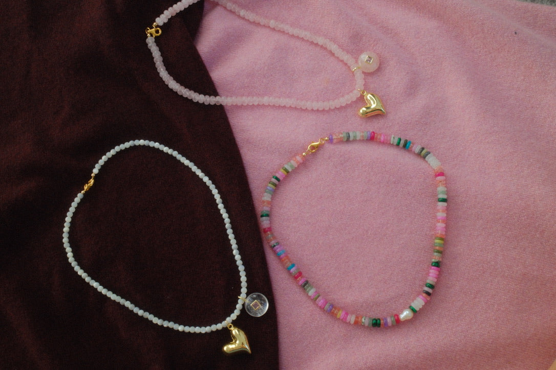 Two necklaces with heart pendants on a pink and brown fabric background
