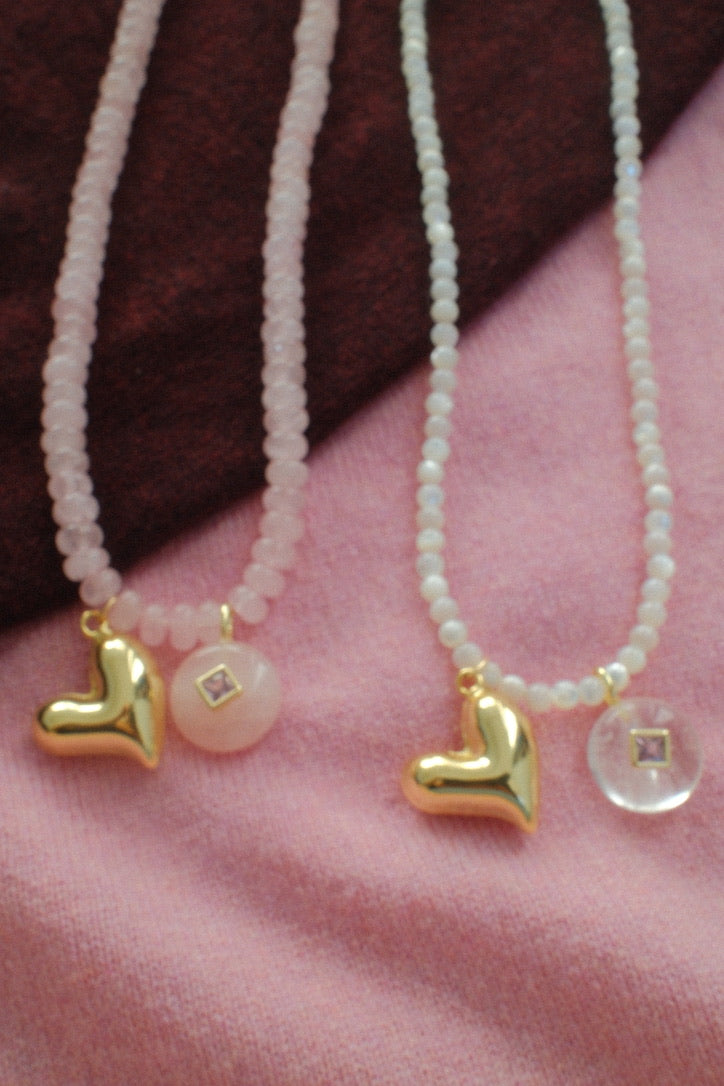 Two pearl necklaces with gold heart pendants on a pink fabric background