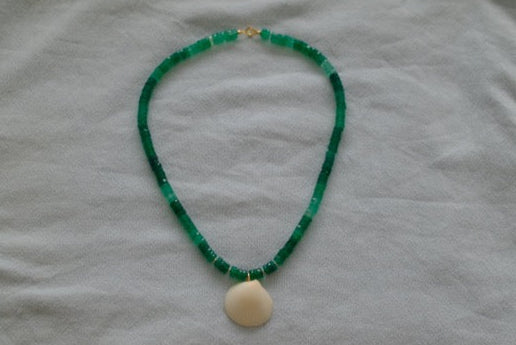 Green beaded necklace with a beige pendant on a light gray fabric background
