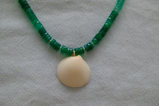 Necklace with green beads and a beige shell pendant on a textured white background