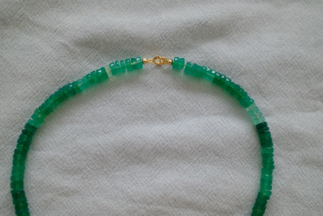 Green beaded necklace with a gold clasp on a light gray fabric background