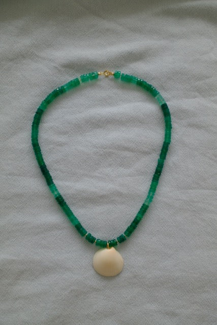 Green beaded necklace with a beige pendant on a light gray background