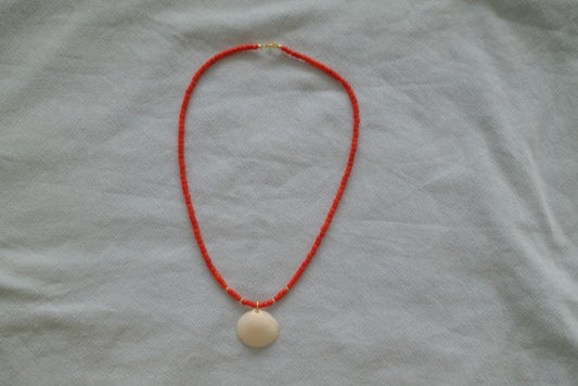 Necklace with a red string and beige pendant on a light gray fabric background