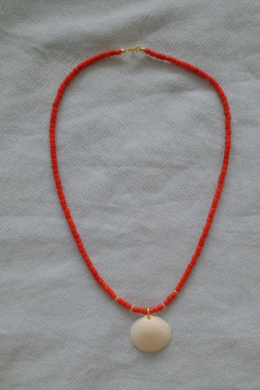 Necklace with red beads and a large shell pendant on a light gray background