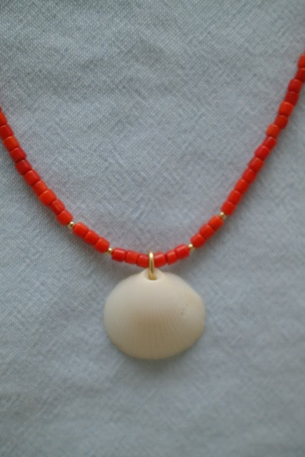 Necklace with red beads and a large beige pendant on a textured gray background