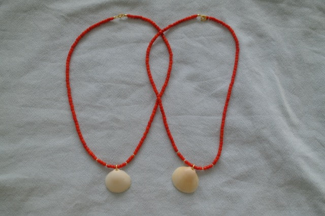 Red beaded necklace with beige shell pendants on a light gray fabric background