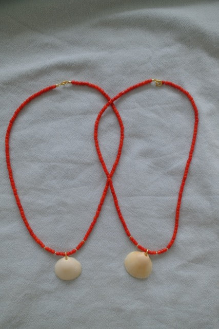 Necklace with red cord and beige shell pendants on a light fabric background