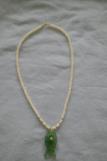 Pearl necklace with a green pendant on a light gray fabric background