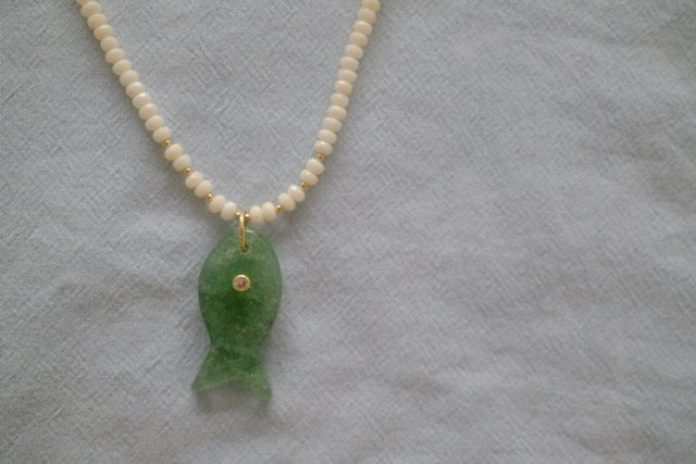 Necklace with a green fish pendant and white beads on a textured gray background