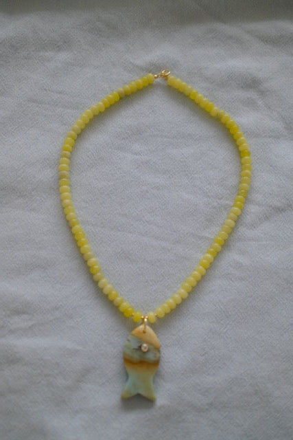 Necklace with yellow beads and a fish-shaped pendant on a light gray background