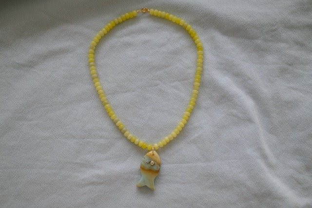 Yellow beaded necklace with a fish pendant on a white fabric background