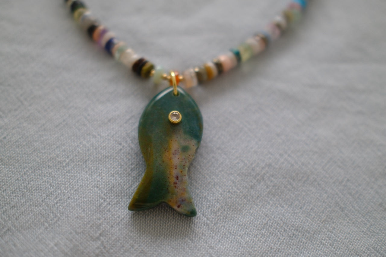 Necklace with a green fish pendant on a textured gray background