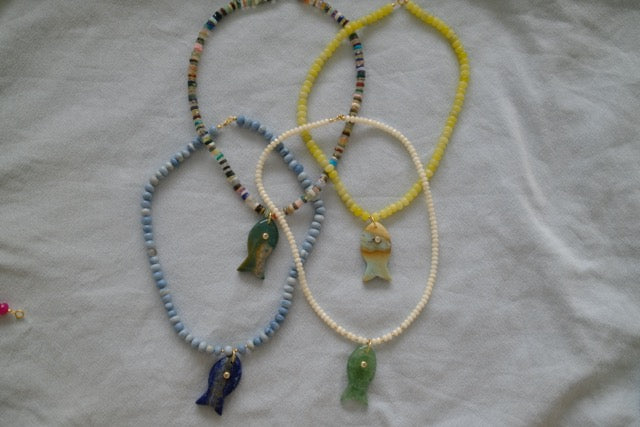 Four necklaces with fish pendants on a light fabric background