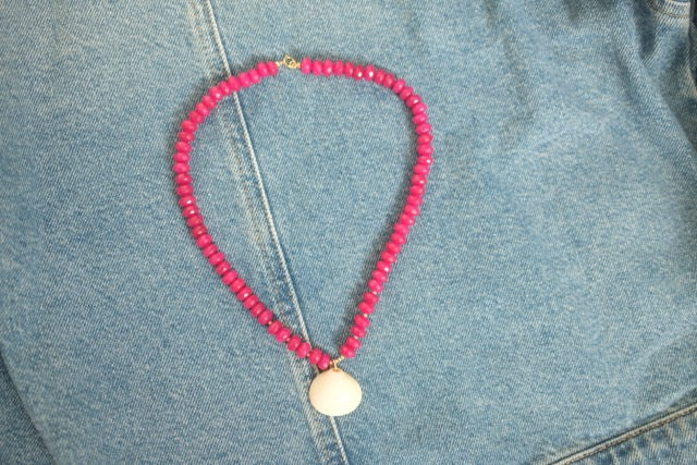 Pink beaded necklace with a gold pendant on denim fabric