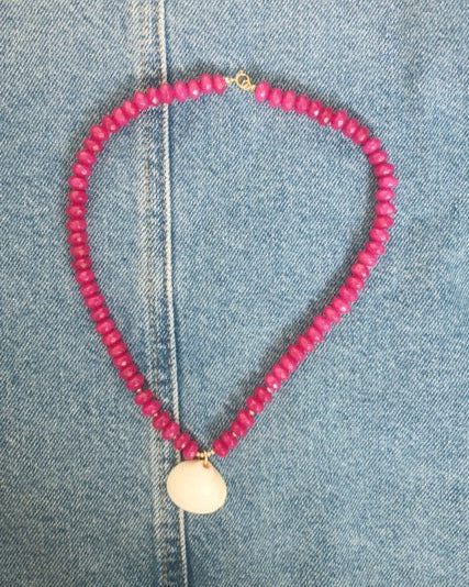 Pink beaded necklace with a gold pendant on denim fabric