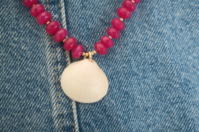 Necklace with pink beads and a white pendant on denim fabric