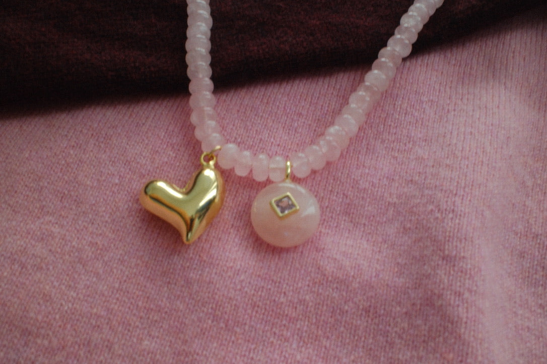 Necklace with heart-shaped and round pendants on a pink fabric background