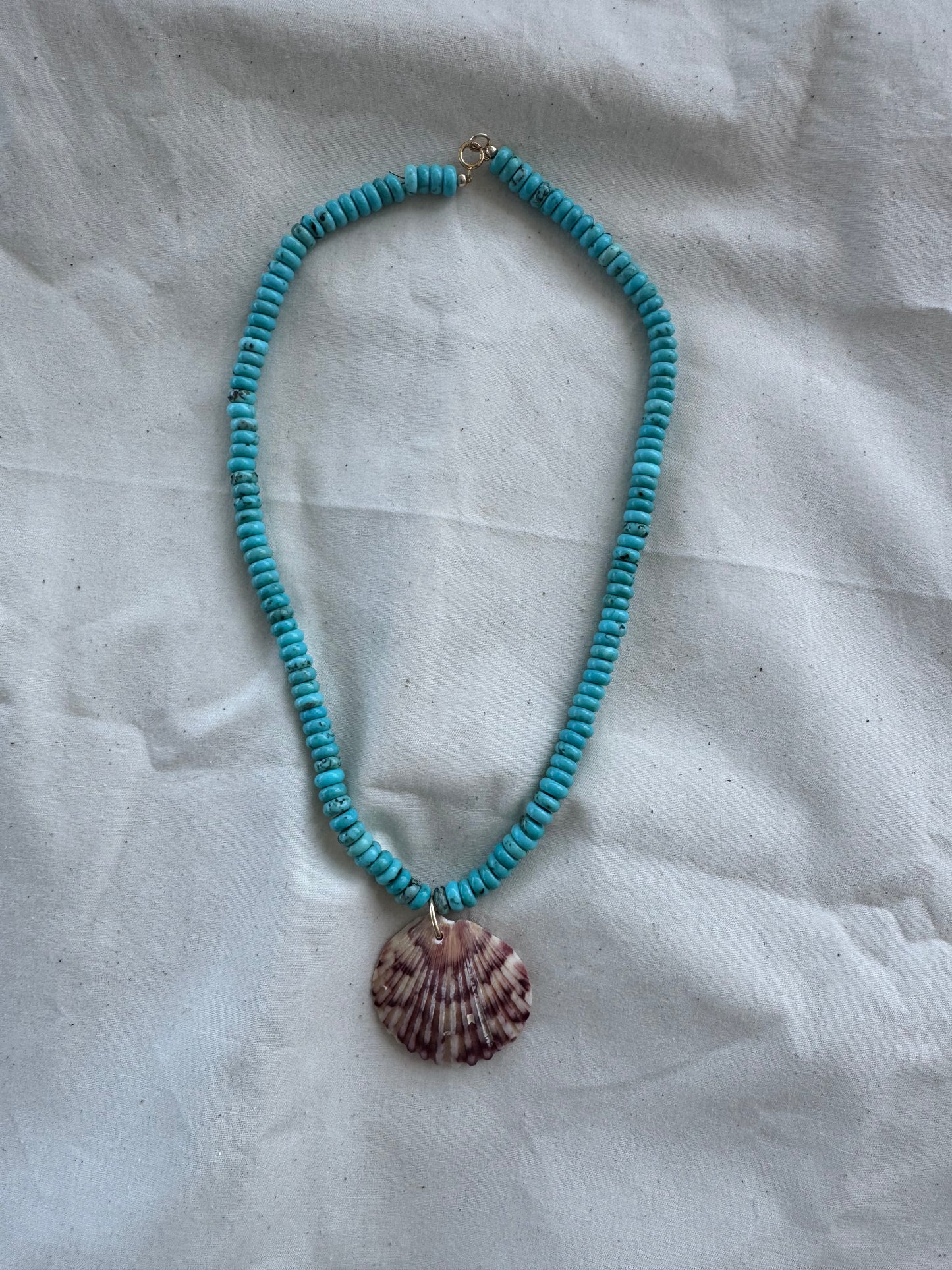 Turquoise beaded necklace with a shell pendant on a textured white surface
