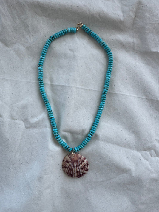 Turquoise beaded necklace with a shell pendant on a textured white surface