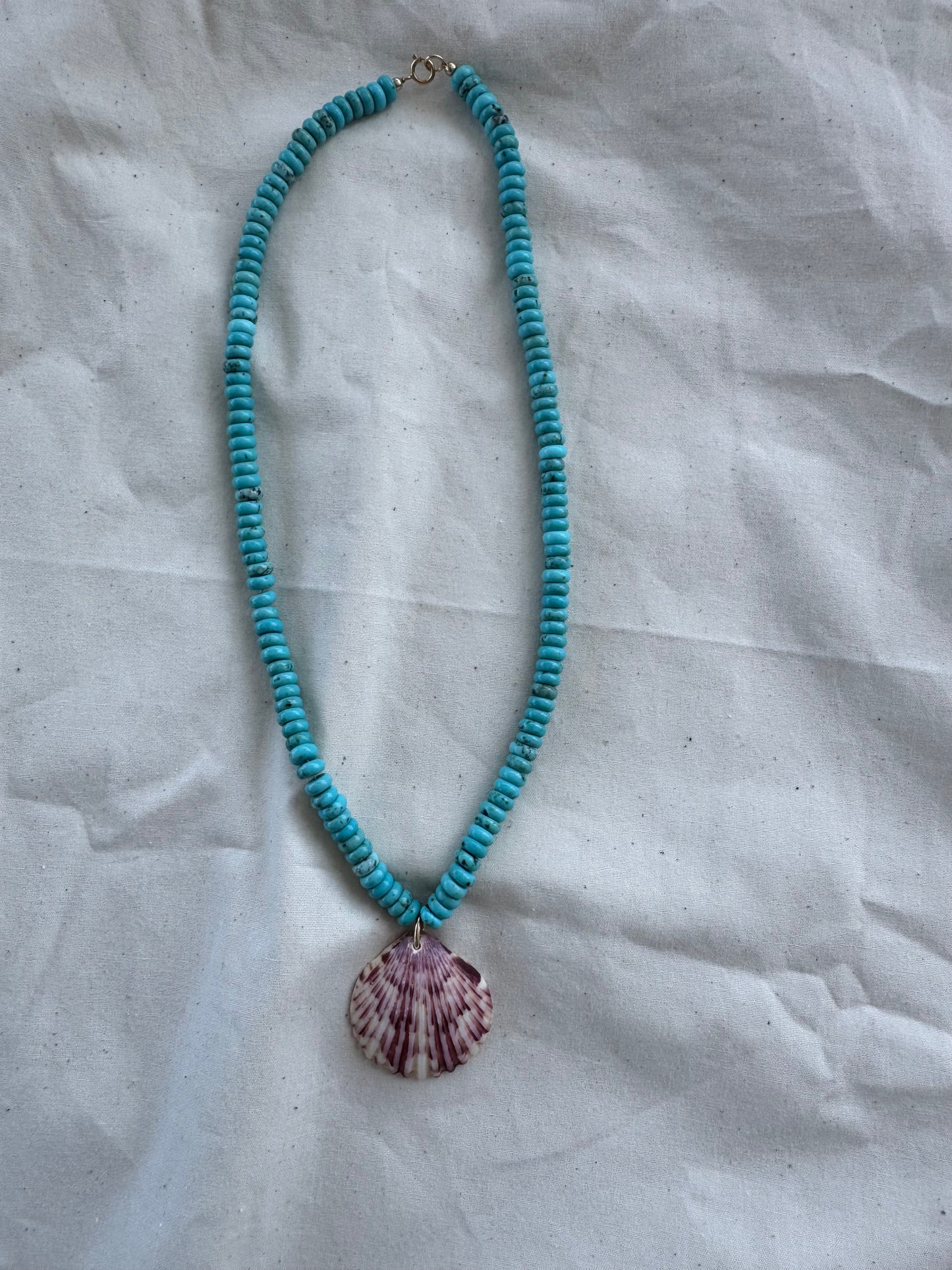 Turquoise beaded necklace with a shell pendant on a textured white background
