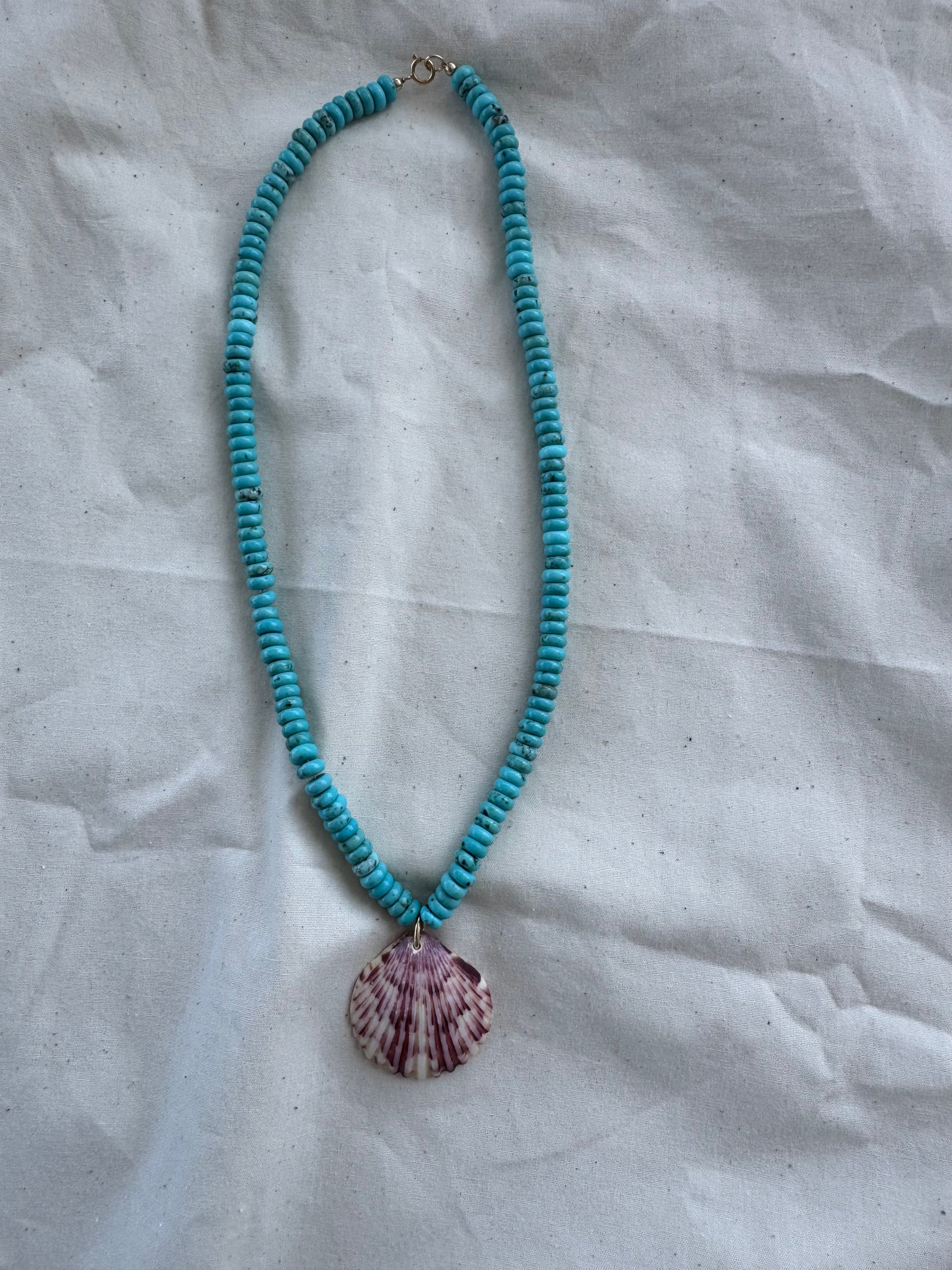 Turquoise beaded necklace with a shell pendant on a textured white background