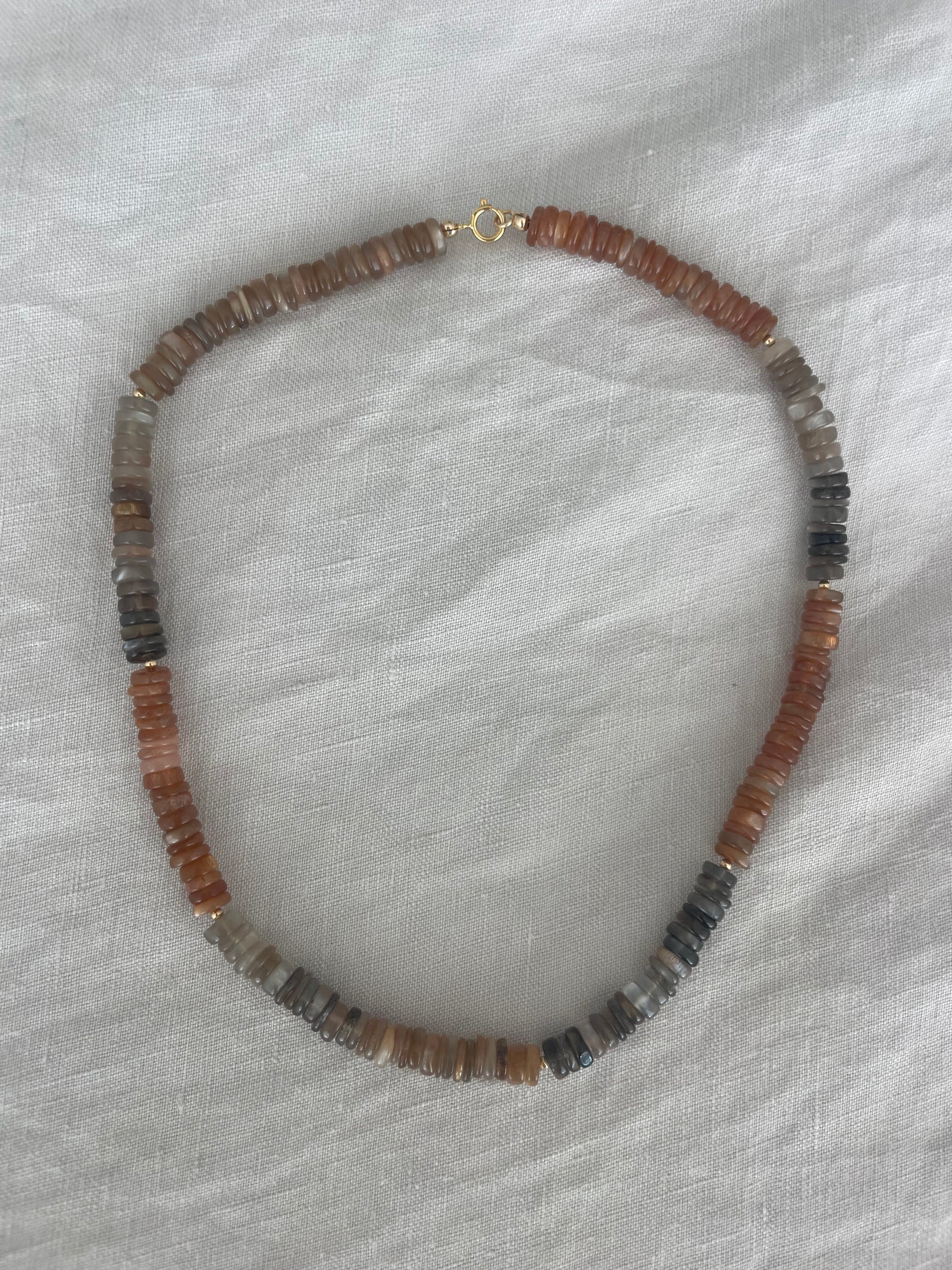 Beaded necklace with brown and black stones on a white fabric background