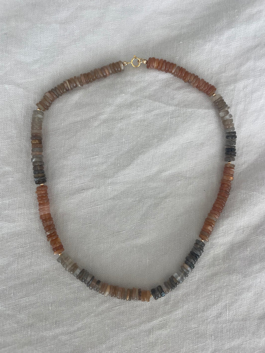 Beaded necklace with brown and black stones on a white fabric background