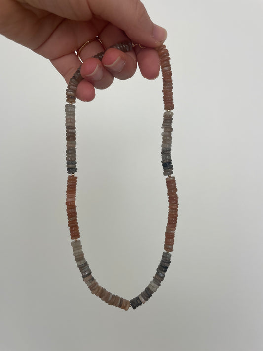 Beaded necklace held by a hand against a plain background