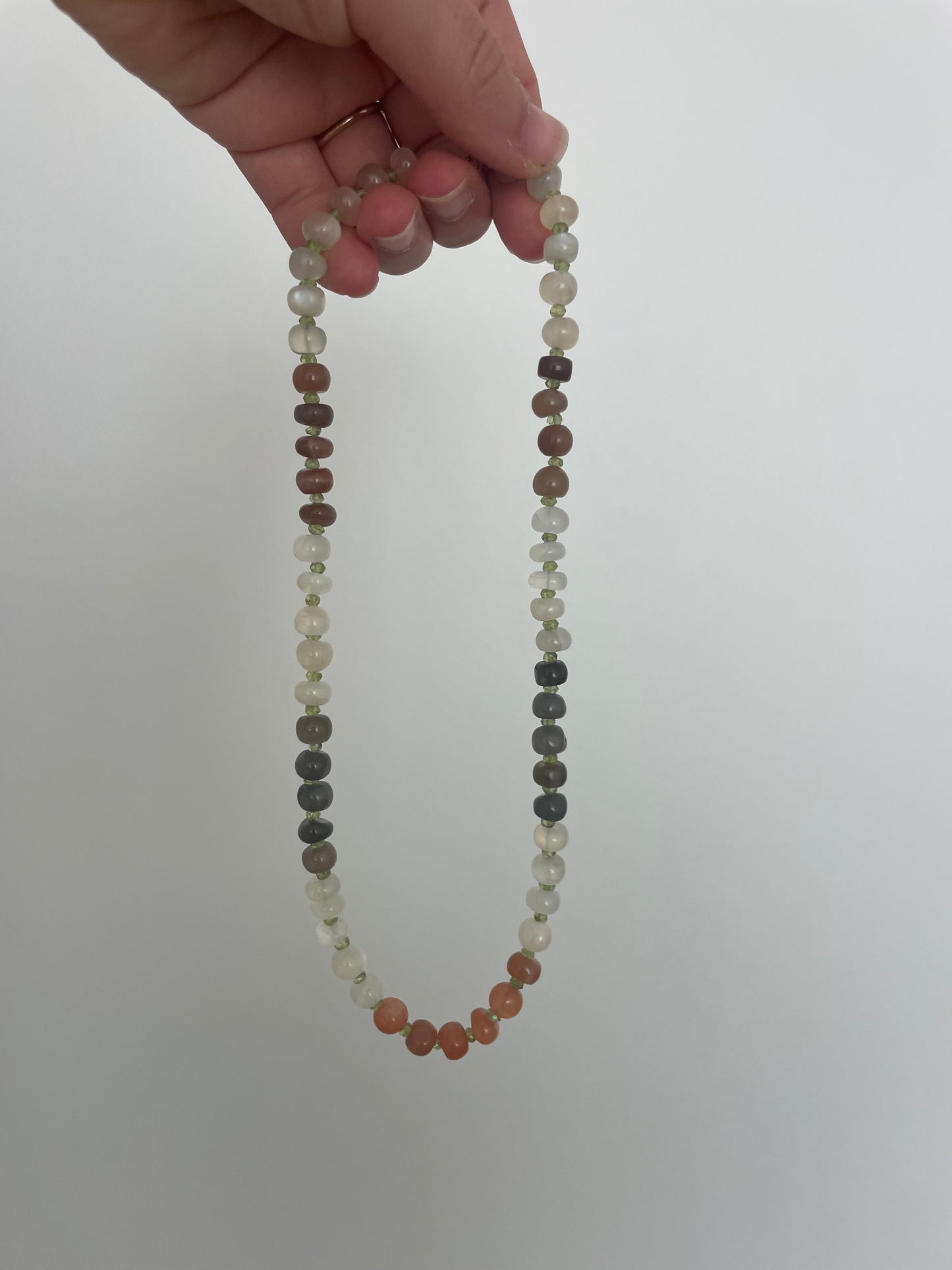 Beaded necklace held by a hand against a plain background