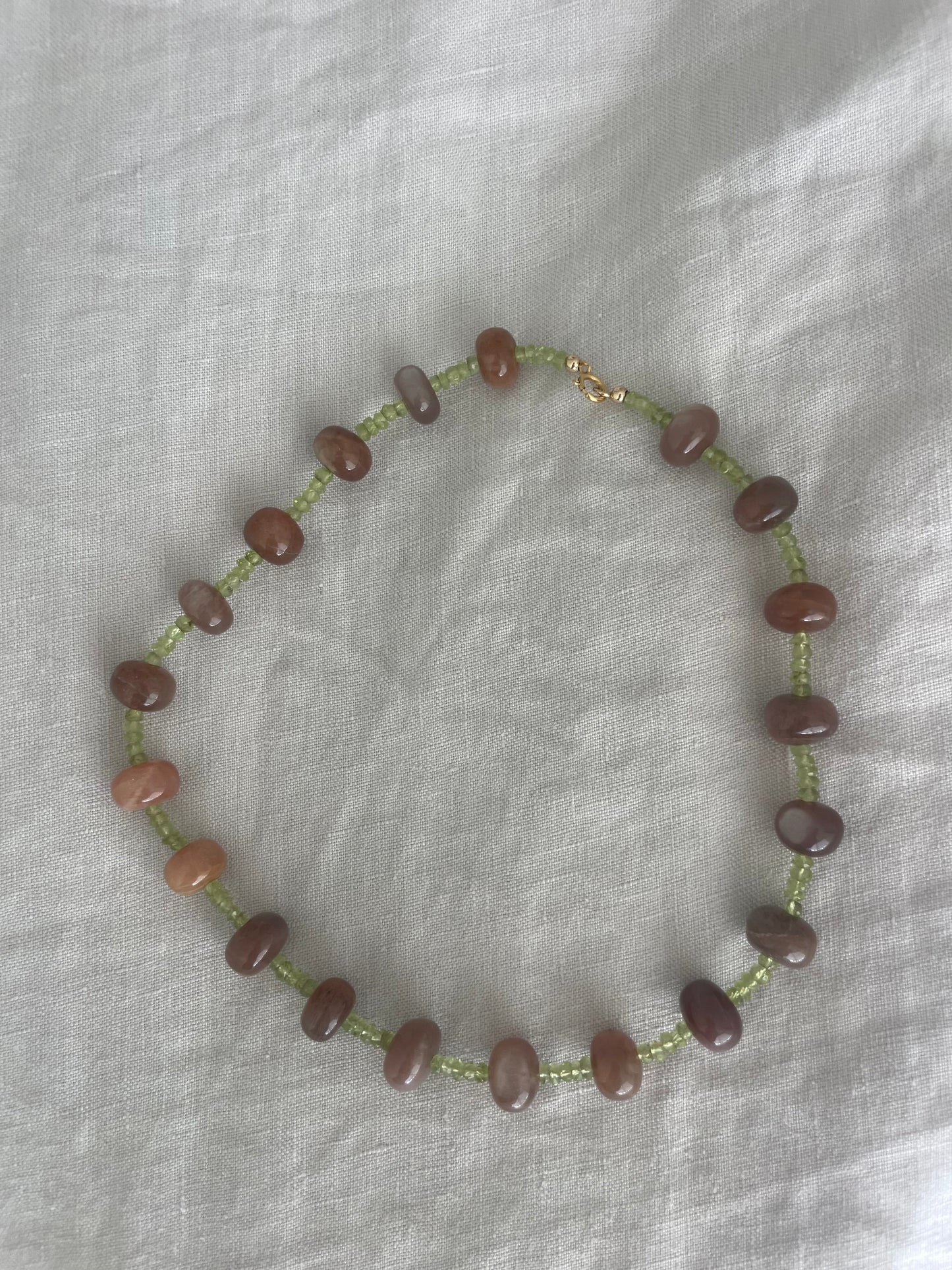 Beaded necklace with brown beads on a green string against a white fabric background