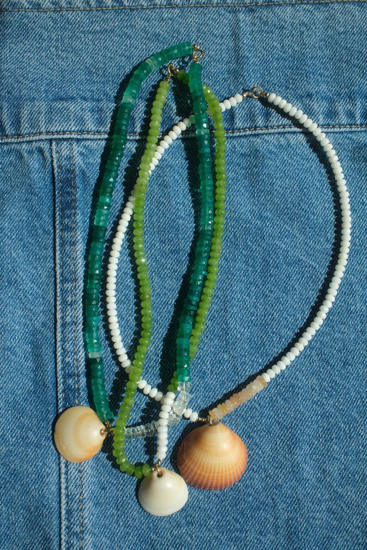Necklace with green, white, and beige beads and shell pendants on a blue denim background