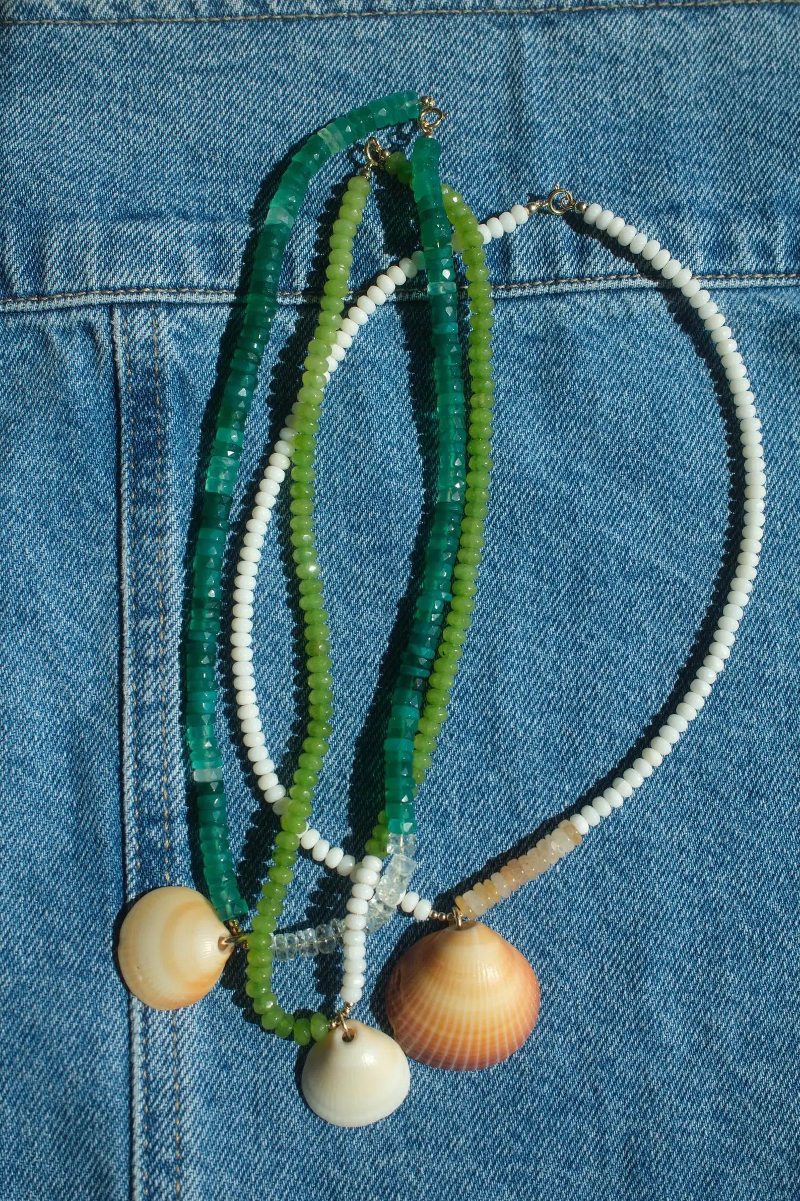 Necklace with green, white, and beige beads and shell pendants on a blue denim background