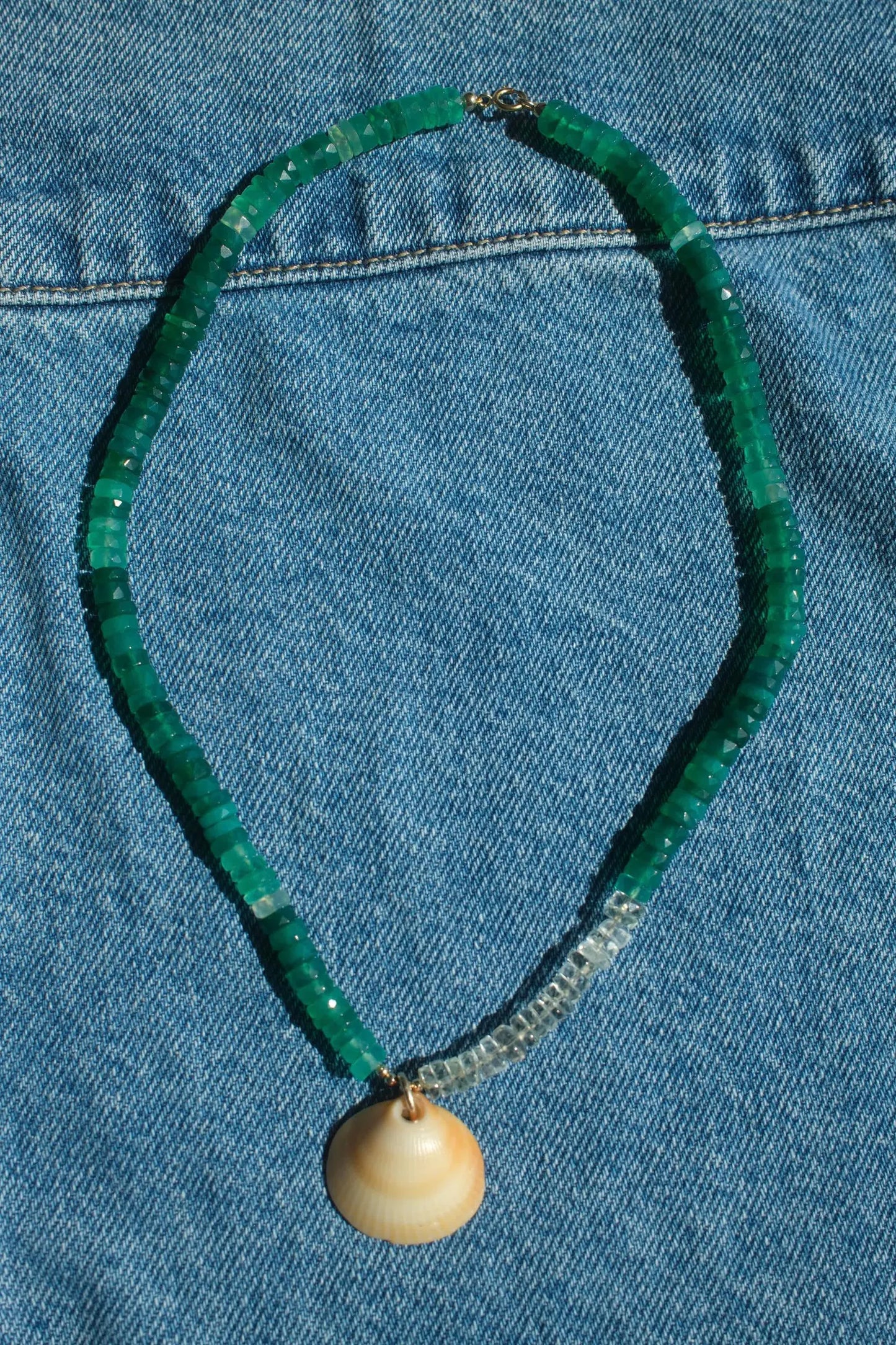 Green beaded necklace with a shell pendant on a blue denim background