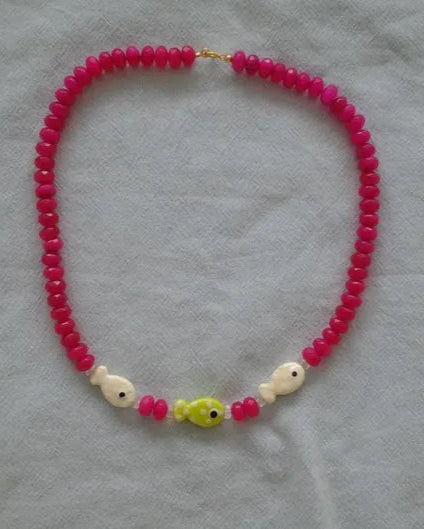 Necklace with pink beads and colorful fish-shaped charms on a light gray background