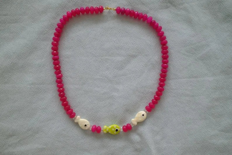 Necklace with pink beads and fish-shaped charms on a light gray background